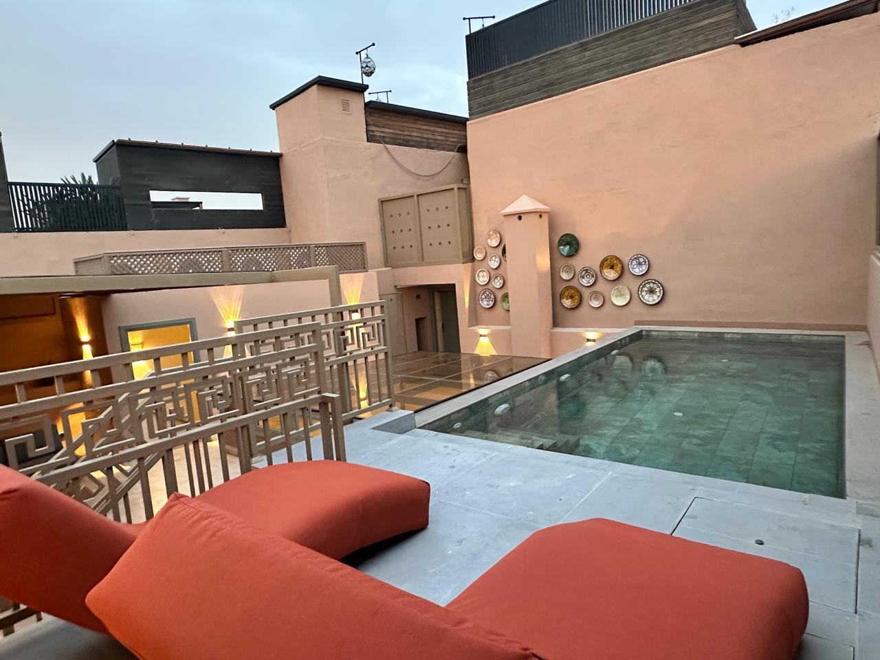 The private rooftop pool, green-tiled, with orange loungers and hand-painted plates on the terracotta wall